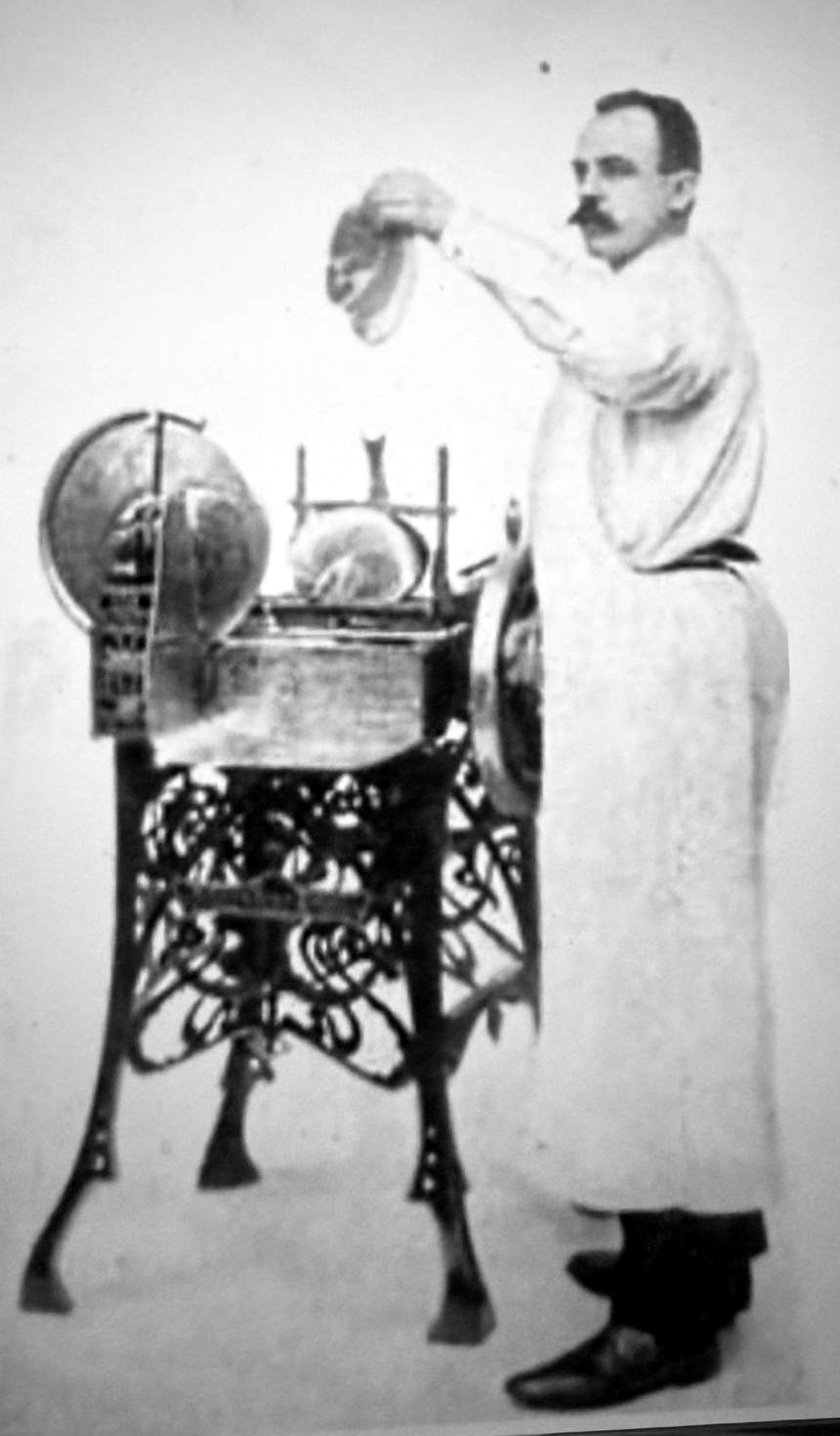 Historische foto van Wilhelmus van Berkel in witte slagersjas naast zijn eerste snijmachine op een sierlijk gietijzeren onderstel